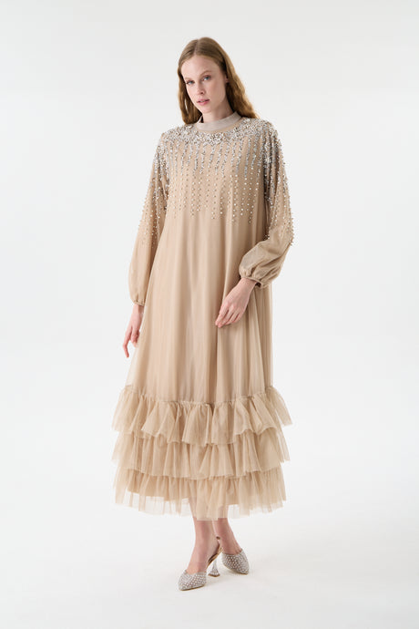 Woman wearing a beige abaya dress with  embellishments on a white background